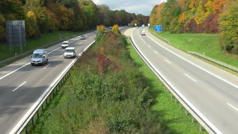 Schnell-Fahrende-Autos-Auf-Einer-Autobahn,-Umrahmt-Von-Wunderschönen-Herbstfarbenen-Bäumen---Dynamisch-Herausgezoomt