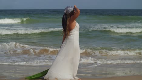 Young-girl-in-a-beach-dress-walks-on-the-beach-with-ocean-waves-in-the-background