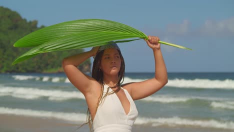Amazing-young-female-shades-under-a-palm-leaf-at-the-beach-with-waves-in-the-background