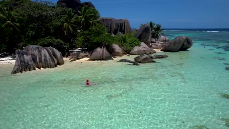Woman-in-Clear-bottom-kayak-floating-next-to-Seychelles-picturesque-tropical-beach-Anse-Source-D'argent-with-palm-tree-and-boulders