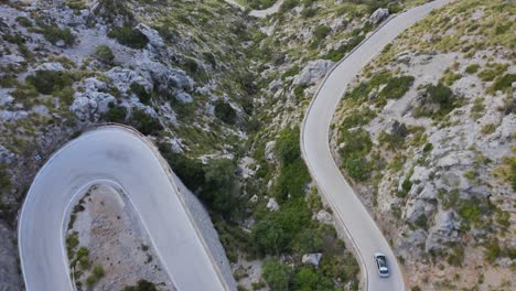 Drone-view-of-a-single-car-driving-down-a-windy-mountain-road-at-Sa-Calobra,-Mallorca,-Spain