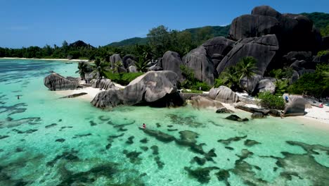 Aerial-Panning-view-of-Iconic-Seychelles-Beach-with-boulders-palm-tree-white-sand-an-woman-in-clear-bottom-kayak