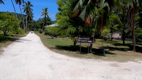 Mujer-De-Rojo-Andando-En-Bicicleta-Por-Un-Camino-De-Tierra-Hasta-La-Playa-De-Anse-Source-D&#39;argent-En-La-Digue-En-Las-Seychelles