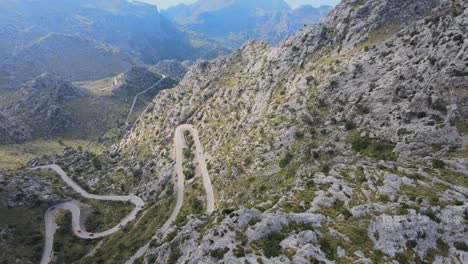 Turning-revealing-drone-shot-of-winding-roads-going-up-a-mountain-with-numerous-hairpin-bends-on-a-sunny-day-at-Sa-Calobra,-Mallorca,-Spain