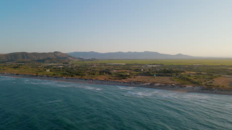 Aerial-view-of-the-coastline-at-Mareny-beach-with-the-rice-fields-and-mountains-in-the-background,-Valencia,-Spain