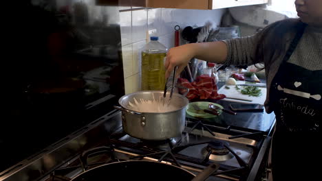 Chef-Femenina-Revolviendo-Fideos-De-Espagueti-Crudos-Dentro-De-Una-Olla-Grande-Con-Agua-Caliente-En-La-Cocina-Dentro-De-La-Cocina