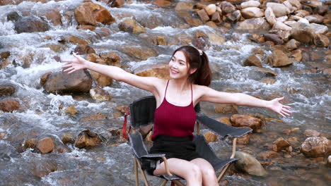 Asian-woman-in-red-sitting-on-a-chair-with-big-rocks-and-water-slow-splashing-for-relaxing-and-happiness-in-the-vacation-summertime