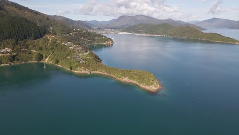 Wide-angle-aerial-dolly-out-of-a-narrow-headland-reaching-out-onto-the-pacific-ocean-with-a-mountain-range-in-the-background-near-Picton,-New-Zealand