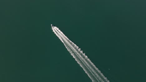 Aerial-top-down-tracking-shot-of-a-speed-boat-riding-straight-over-turquoise-green-ocean-water