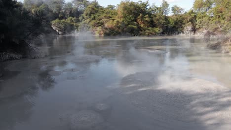 Slow-motion-dolly-in-flying-low-over-splashing-mud-explosions-at-Waiotapu,-New-Zealand