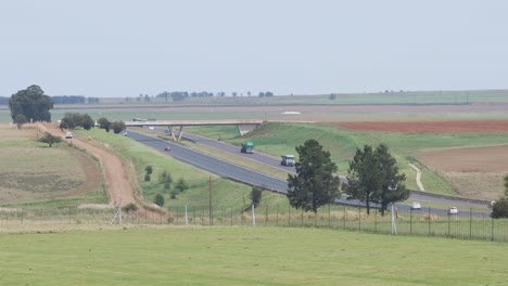 A-shot-overlooking-agricultural-farmland-on-to-the-N4-National-highway-with-a-number-of-passenger-vehicles,-coal-and-logistics-trucks-passing-by-travelling,-Mpumalanga,-South-Africa