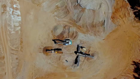 Aerial-top-down-shot-of-working-excavator-digging-sand-at-sand-quarry-during-sunny-day---orbit-shot
