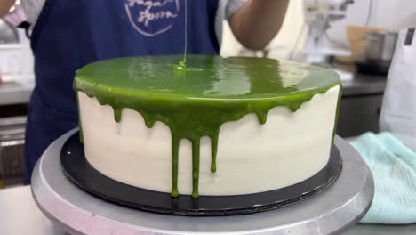 Spinning-the-turntable-to-smooth-out-the-matcha-chocolate-mirror-glaze,-close-up-shot
