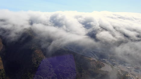 Fog-rolling-in-over-the-mountain-landscape-along-the-west-Coast-in-Brisbane,-California---dynamic-aerial-view
