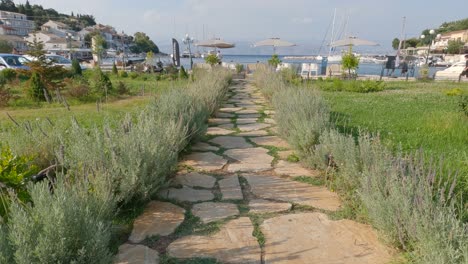 Tilt-Up-Shot-From-Rustic-Garden-Path-Leading-To-promenade-With-Parasols-In-Kassiopi,-Corfu