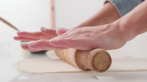Using-a-rolling-pin-to-flatten-the-dough,-preparing-food-on-a-kitchen-table