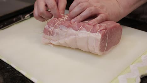 Butcher-is-tying-up-a-piece-of-pork-loin-meat,-tying-it-to-prevent-from-spreading