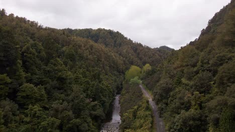 Drone-Siguiendo-Un-Río-De-La-Selva-Junto-A-Una-Carretera-Estrecha-Que-Atraviesa-Un-Valle-De-Montaña