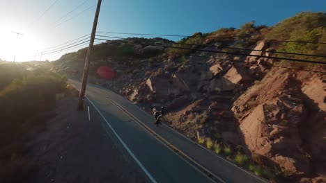 Motorcycle-Stunt-rider-silhouette-along-Winding-road-chase-by-Fpv-drone,-Topanga-California