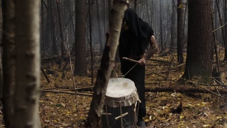 Mysterious-man-playing-music-with-a-rustic-homemade-drum-in-the-middle-of-the-forest