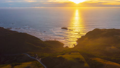 Aerial-sweeping-time-lapse-of-the-sun-setting-over-the-Pacific-Ocean,-showing-the-coastal-countryside-on-the-island-of-Chiloe,-beautiful-sunset