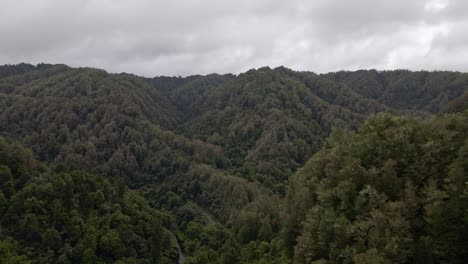 Aerial-crane-shot-of-a-dense,-mountainous-rainforest-underneath-an-overcast-sky
