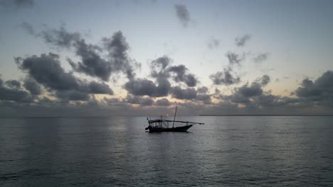 Silhouette-of-fishing-boat-Uroa-beach-Zanzibar-Island-floating-near-the-shore-during-sunset,-Aerial-hovering,-shot