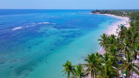 Beautiful-Aerial-View-Of-Playa-Guayacanes-Surrounded-By-Clear-Blue-Sea-And-White-Sand-Lined-With-Palm-Trees-In-Santo-Domingo,-Dominican-Republic