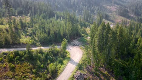 Three-vans-camping-at-the-edge-of-a-hairpin-turn-along-an-empty-logging-road-within-a-partially-logged-coniferous-forest-in-British-Columbia,-Canada