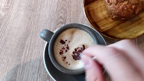 POV-of-having-a-cappuccino-and-a-muffin-in-a-café,-hand-stirring-the-coffee-with-small-teaspoon