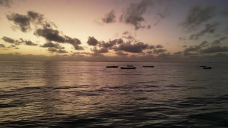 Small-fishing-boats-in-shallow-waters-at-Uroa-beach-Zanzibar-Island-during-sunset,-Tanzania-Africa,-Aerial-flyover-shot