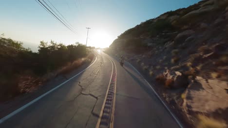 Fpv-Drone-Flyover-Topanga-Sinuoso-Camino-Sigue-Motociclista-Truco-Mientras-Hace-Un-Caballito,-Luz-Solar-Brillante,-California