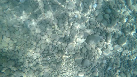 Meeresboden-Bedeckt-Mit-Steinen-Und-Felsen-Mit-Wunderschönen-Sonnenlichtreflexionen,-Die-Sich-Bewegen-Und-Verschiedene-Formen-Annehmen
