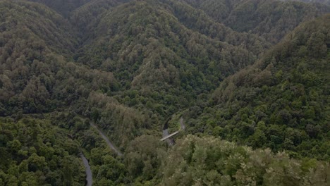 Aerial-establishing-shot-of-a-tiny,-old-river-bridge-within-a-pristine,-mountainous-rainforest