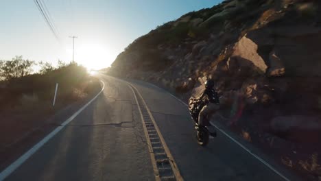 Immersive-Fpv-view-from-Drone-following-Stunt-rider-perfroming-wheelie-on-Asphalt-winding-road,-Topanga,-California