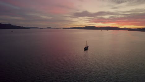 Aerial-shot-of-a-small-boat-anchored-at-sea-with-a-stunning-sunset