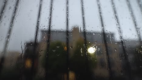 An-abstract-close-up-shot-of-a-window-covered-in-rain-droplets,-as-more-rain-falls-the-water-runs-down-the-window-on-a-dark-grey-gloomy-day-during-thunderstorm-lightning