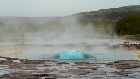 People-Walking-By-Erupting-Geyser-Strokkur-In-Geothermal-Area-In-Iceland