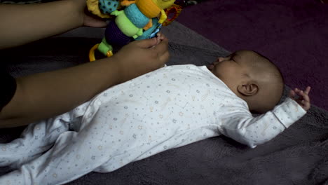 Adorable-2-Month-Old-Indian-Baby-Boy-Laying-On-His-Back-Being-Entertained-By-Colourful-Plush-Toy