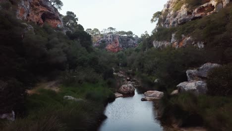 Aerial-fpv-flight-over-river-with-rocks-in-ravine-with-bright-sky-at-sunset