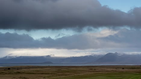 Time-lapse-shot-of-flying-clouds-at-sky-over-Iceland-landscape-and-snowy-mountains-in-background