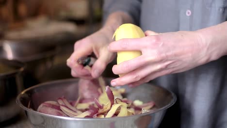 peeling-potato-with-a-knife-in-a-bowl-in-the-kitchen-with-people-stock-video-stock-footage