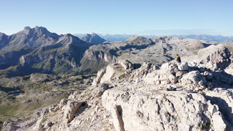 Alpine-climber-sitting-on-mountain-peak-in-Dolomites,-aerial-view