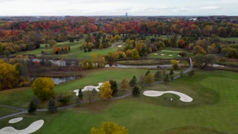 Fly-over-a-golf-course-surrounded-by-a-park-in-a-fall,-cloudy,-moody-day