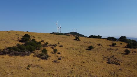 Renewable-energy-windmill-farm-on-top-of-hill,-aerial-fly-away-view