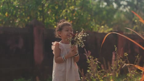 Static-handheld-shot-of-a-laughing-girl-in-the-garden-while-holding-a-bouquet-of-flowers-in-her-hands-with-plants,-trees-and-a-stone-wall-in-the-background