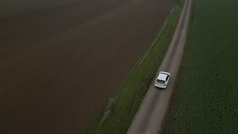 Single-white-car-driving-country-road,-drone-following-view,-autumn-cloudy-weather