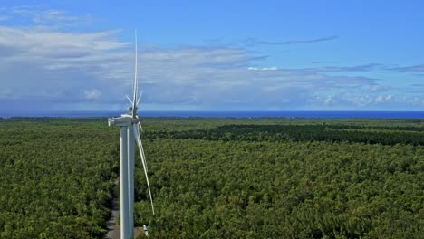 Side-drone-view-of-line-of-wind-turbines-in-lush-forest-landscape,-pretty-sky