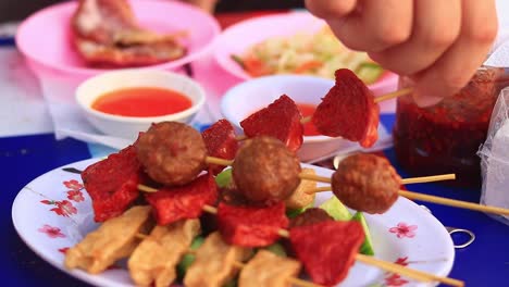 Nahaufnahme-Eines-Tellers-Voller-Khmer--Oder-Kambodschanischer-Streetfood-Spieße,-Während-Ein-Tourist-Sie-Probiert