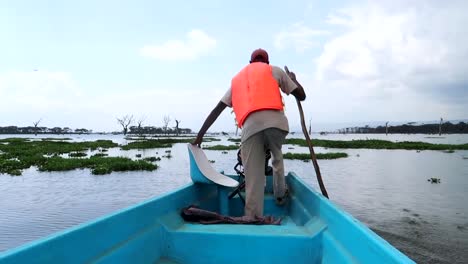 African-man-rowing-with-a-stick-in-a-blue-fiber-boat-leaving-Crescent-Island,-Kenya